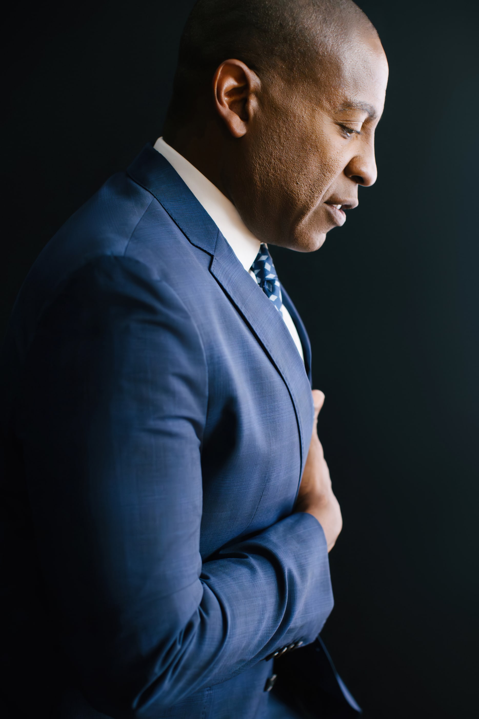 Carlos Watson in profile, head bowed, in a blue suit